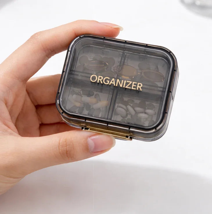 Hand holding clear pill organizer with labeled compartments for daily medication storage