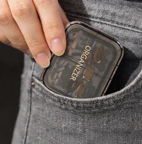 Portable pill organizer with clear lid, holding capsules, tucked in jeans pocket for on-the-go use