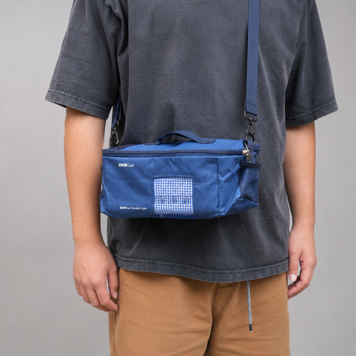 Person wearing a blue crossbody bag with a cooler in it standing against a gray background