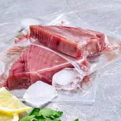 Vacuum-sealed raw tuna steaks with ice cubes and lemon slices on a marble surface